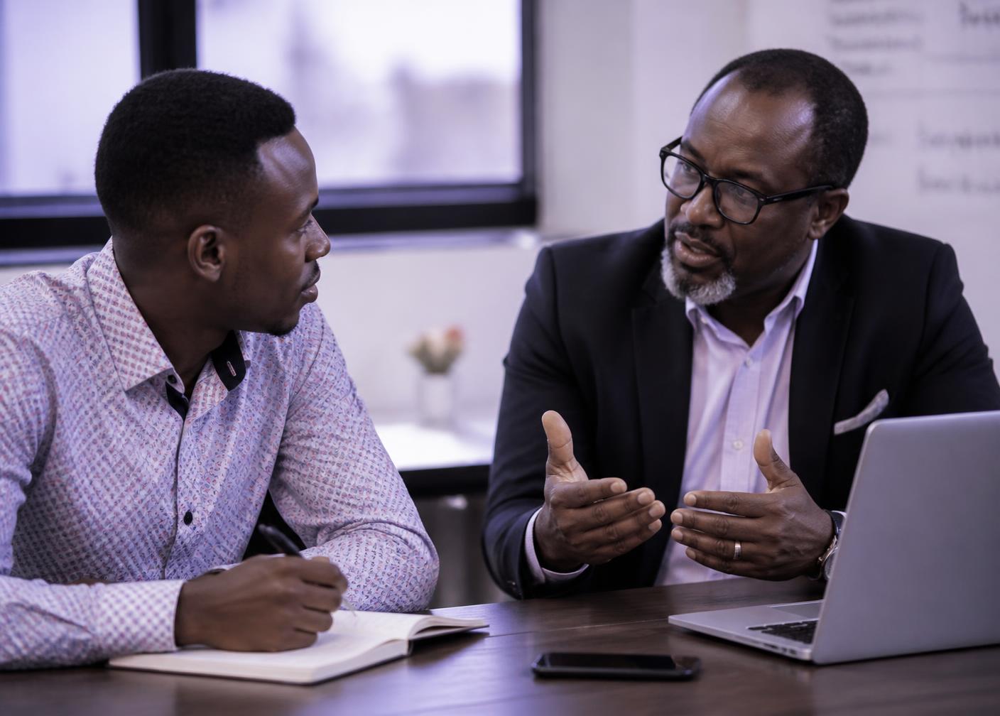 An experienced professional giving feedback to a younger colleague at a desk